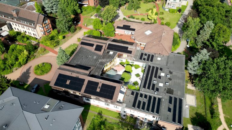 Luftaufnahme des Altenwohnhauses der Stiftung Haus Zuflucht in Soltau, schwarze Photovoltaikmodule auf den Ziegeldächern und auf der Flachdachfläche des Innenhofgebäudes, ringsum Gartenanlagen und weitere Wohngebäude