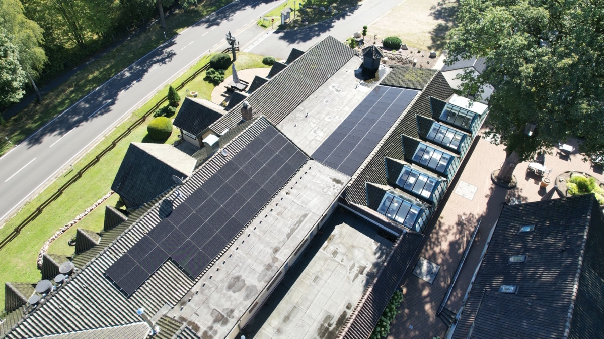 Luftaufnahme des Dachs von Hof Barrl mit schwarzen Photovoltaikmodulen auf zwei Dachflächen, rechts die Glasgauben des Wintergartens, links die am Grundstück vorbeiführende Straße.