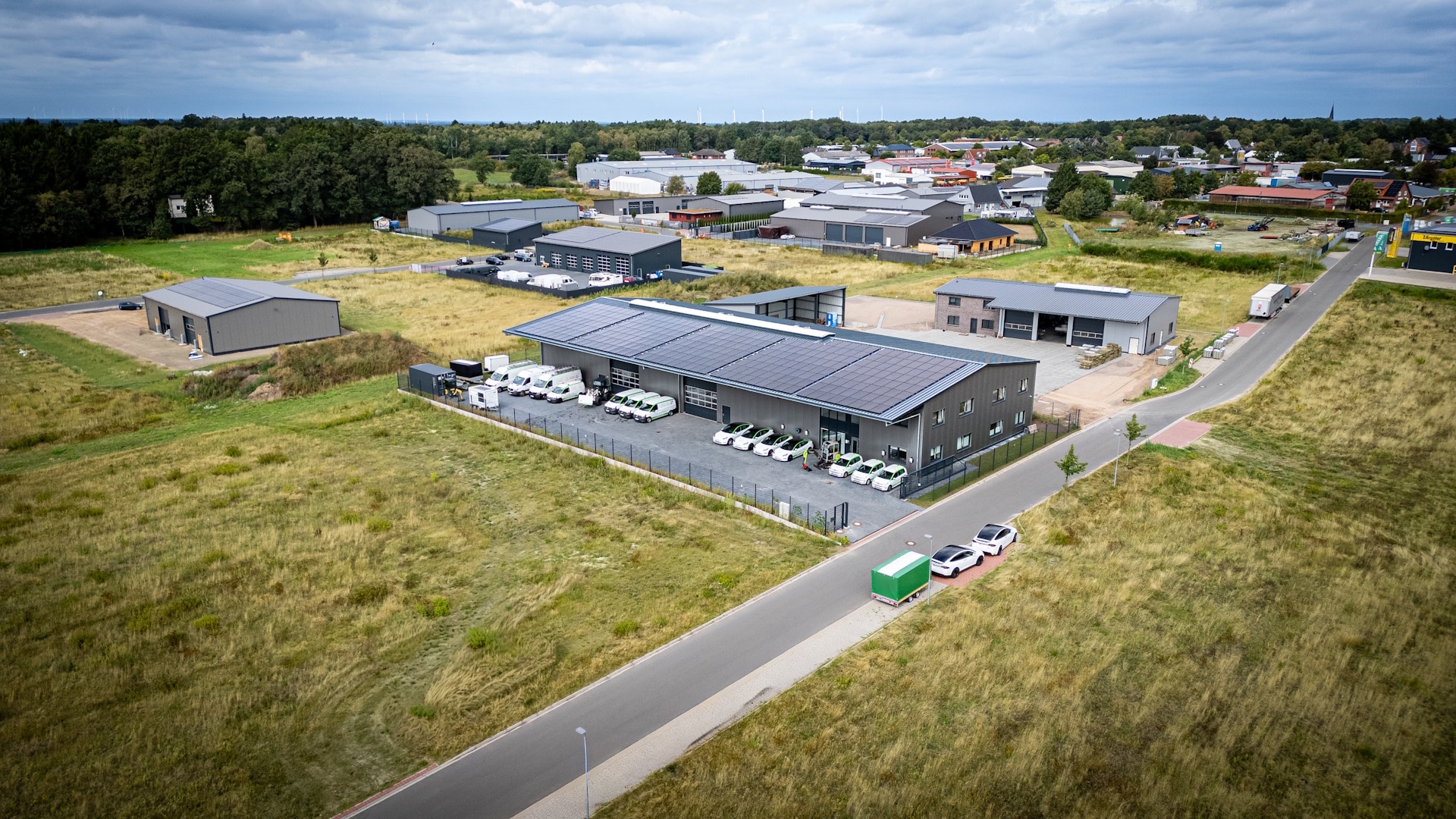 Luftbild des Firmensitzes der INOL GmbH im Gewerbegebiet. Auf dem langgestreckten Hallendach liegen Photovoltaikmodule, davor stehen weiße Fahrzeuge mit grüner Beschriftung auf gepflastertem Hof.